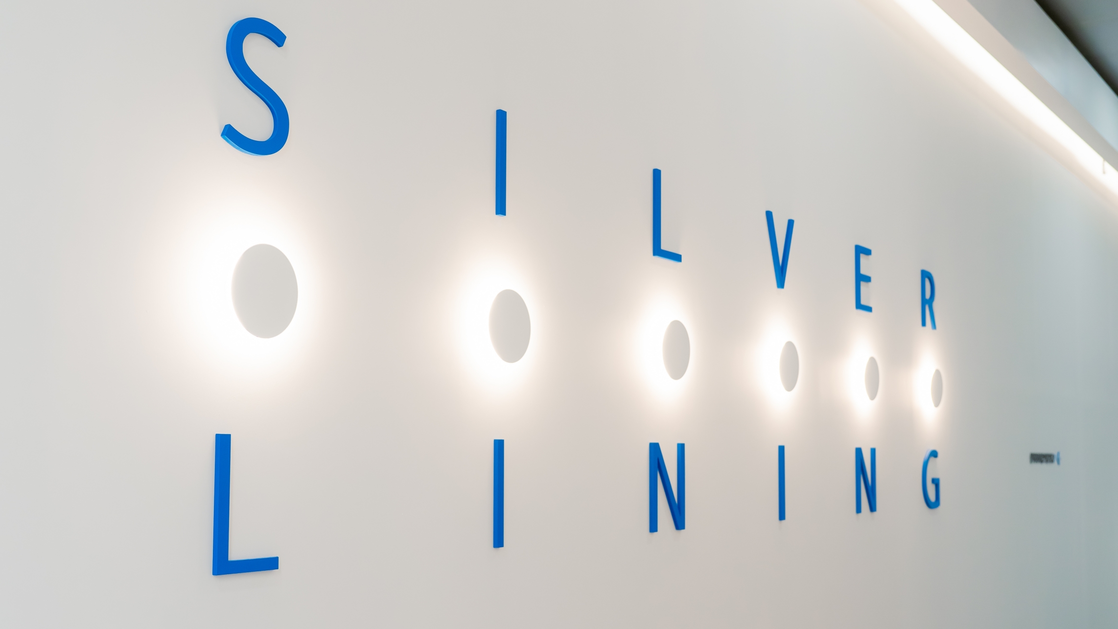 화이트 벽면에 블루 컬러 입체 글씨와 원형 간접조명으로 연출된 실버라이닝(SILVER LINING) 로비 사인 이미지