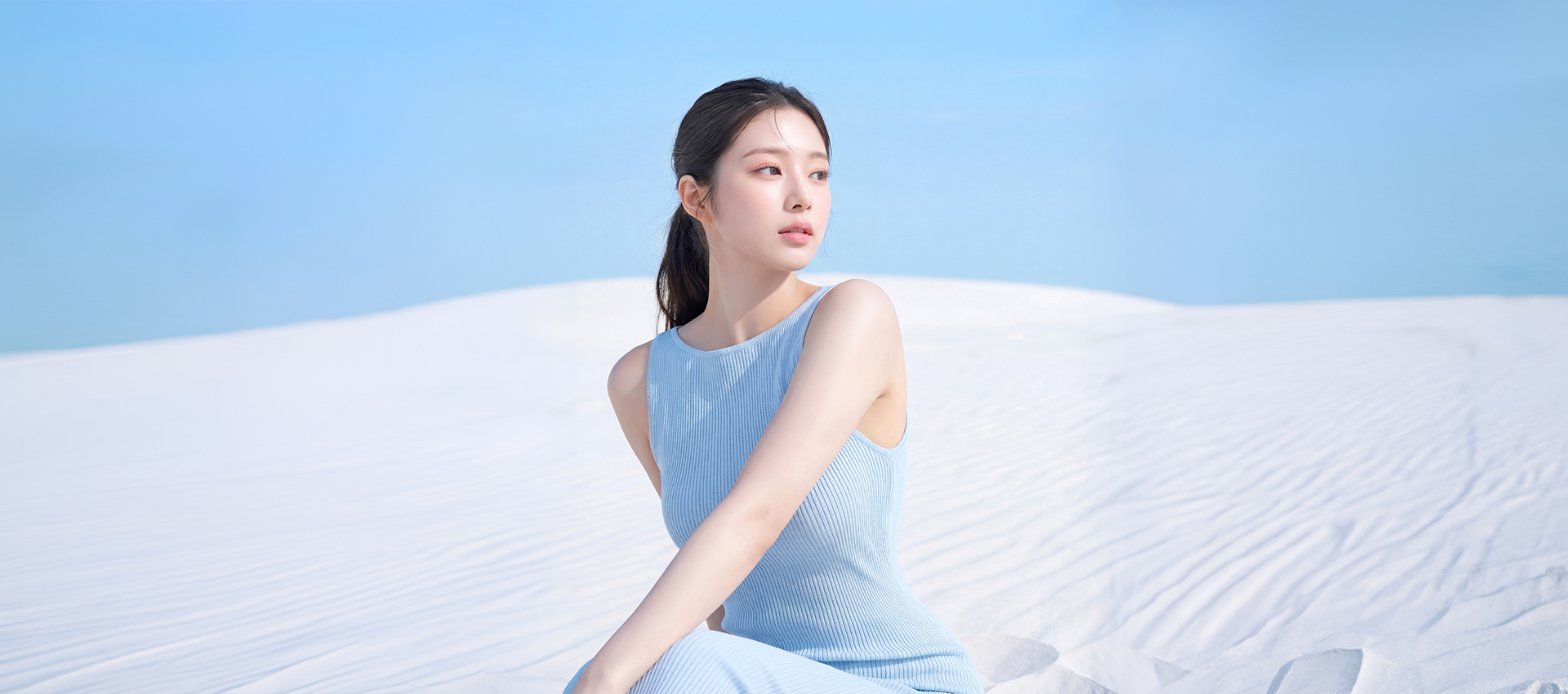 하얀 모래 언덕을 배경으로 앉아있는 매끄러운 바디 라인의 여성 이미지
