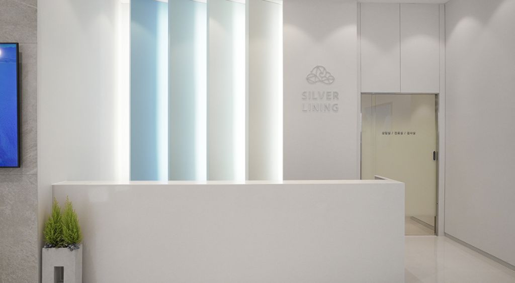 SILVER LINING 로고와 블루 톤 조명이 돋보이는 실버라이닝의원 접수 벽면 및 벨트